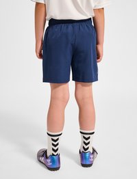 Mörkblå atletiska shorts med elastisk midja, tillsammans med vita strumpor med svart chevronmönster och lila fotbollsskor.