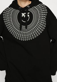 Černá mikina s kapucí s kruhovým bílým grafickým designem obsahujícím opakující se text a centrální logo. Směs bavlny, vybavená stahovací kapucí.