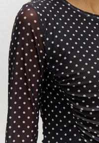 Zwarte mesh top met lange mouwen, voorzien van witte stippen, gathering aan de zijkanten en een ronde halslijn. Zachte textuur.