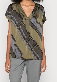 Olivegrön blus med V-ringning, korta ärmar och oregelbundna svarta och grå randiga mönster. Slät tyg med en drapérad passform.