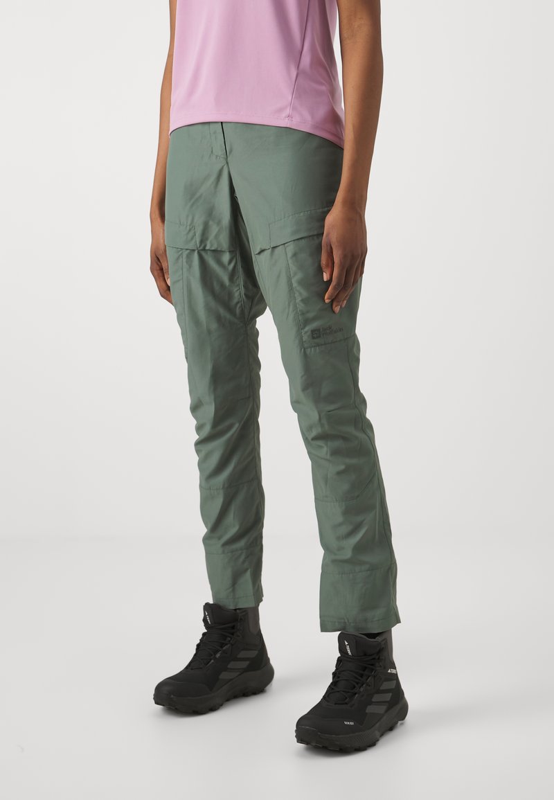 Pantalons cargo légers verts avec plusieurs poches, une coupe décontractée et des détails cousus, associés à des bottes de randonnée noires.