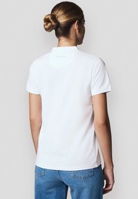 Biała koszulka polo z krótkim rękawem, złożonym kołnierzykiem i prostym designem. Posiada subtelne logo marki w pobliżu szyi oraz gładką teksturę.