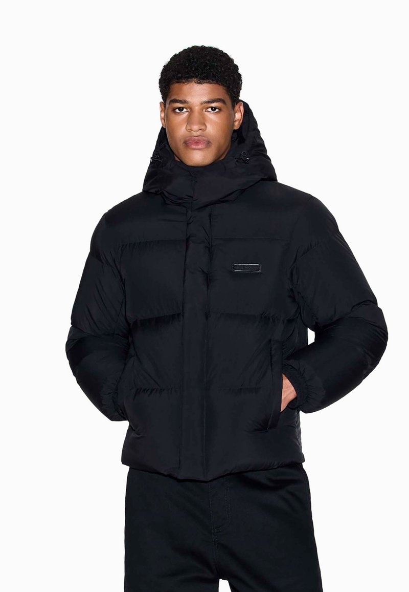 Schwarze Pufferjacke mit Kapuze, mit Reißverschluss, elastischen Bündchen und Fronttaschen. Glatte Textur mit sichtbaren Nähten und Logodetails.