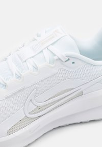 Gros plan sur une paire de chaussures de course Nike blanches avec des panneaux en maille, une semelle texturée et le logo swoosh emblématique sur le côté.