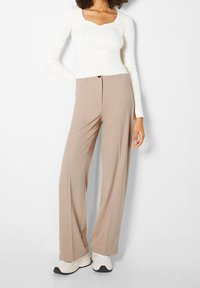 Beige brede broek met een gladde stof en een hoge taille, gecombineerd met een witte geribbelde lange mouw top en witte sneakers.