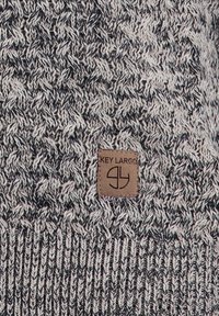 Gestickter Pullover mit einem strukturierten grau-schwarz Muster, einem gerippten Saum und einem gebrandeten hellbraunen Lederetikett.