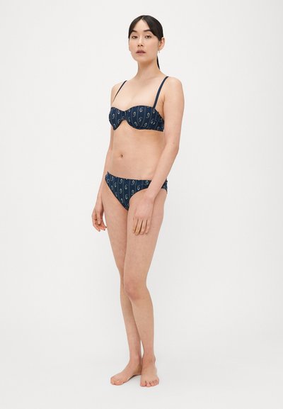 Tengerészkék bikini szett mintás kialakítással. Strukturált alátámasztású felsőrésszel és félig hipster fazonú alsóval, oldalán ráncolt részletekkel. Vékony vállpántokkal.