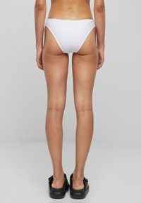 Biele bikiny nohavičky s vysokým strihom a minimálnym pokrytím, vyrobené z hladkej tkaniny s čistým zakončením.