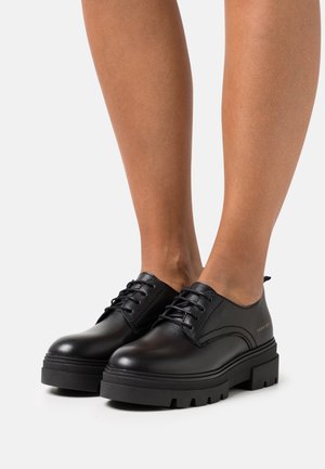 Chaussures en cuir noir à lacets avec un bout arrondi, une semelle épaisse texturée et des détails de coutures minimalistes. Design compact avec une finition mate.