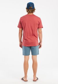 T-shirt en coton rouge à manches courtes, assorti à un short bleu, affichant une coupe décontractée et de subtils détails de couture. Accompagné de tongs.