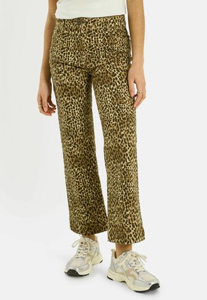 Pantalones de pierna ancha con estampado de leopardo usados con zapatillas blancas, visibles desde la cintura hasta los pies sobre un fondo liso.