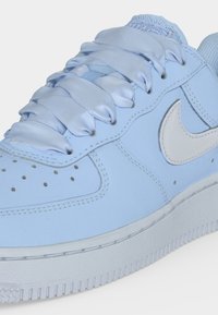 Close-up of a light blue sneaker with glossy satin laces and a white Nike swoosh logo on the side.