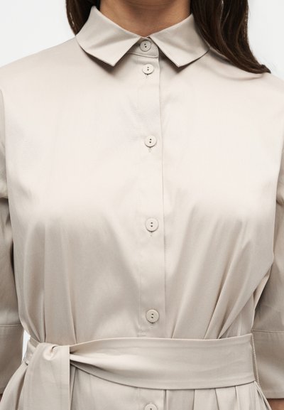Robe beige à boutons avec col, manches mi-longues et ceinture nouée à la taille.