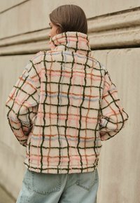 Pulover din fleece pufoasă în nuanță de crem, cu un model în carouri multicolore. Are linii verzi, roz, albastre și maronii; guler înalt; croială relaxată.