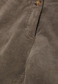 Tissu en velours côtelé marron avec couture visible et un bouton marron près de l'ouverture d'une poche.