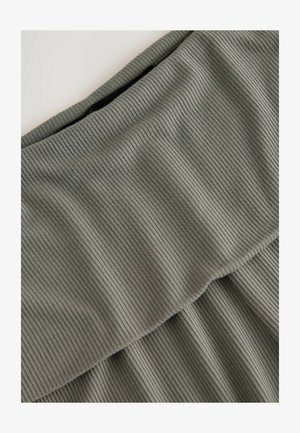 Tessuto a coste e morbido in verde tenue. Presenta una vita piegata e una texture stratificata. Il design enfatizza le linee orizzontali e una sottile profondità.