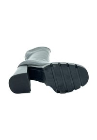 Bota negra hasta la rodilla con parte superior de cuero liso, tacón cuadrado y suela de goma texturizada con surcos horizontales para mayor tracción.