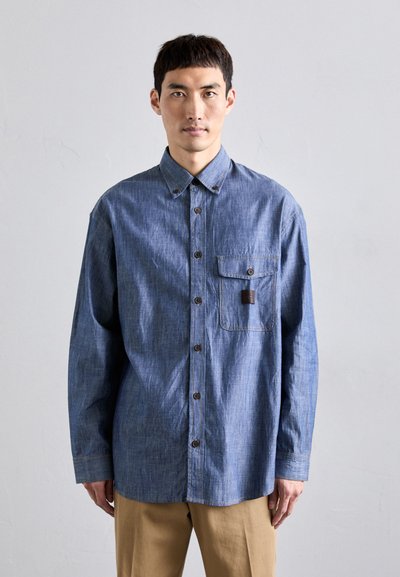 Denim-painattu nappipaita keskipunaisena, jossa on rintatasku, klassinen kaulus ja erottuva ommel. Pitkät hihet, joissa on rento istuvuus.