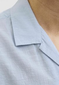 Camisa de cuello azul claro con un diseño sencillo; hecha de una tela texturizada, que cuenta con un cuello tradicional y detalles de costura limpios.