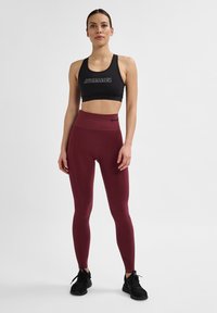 Schwarzer Sport-BH mit Logo, kombiniert mit hochgeschnittenen burdeos-farbigen Leggings. Die Leggings haben eine glatte Textur und eine dehnbare Passform, die sich gut für Sport eignet.