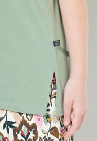 Lichtgroene t-shirt met korte mouwen en zijsplitten, gecombineerd met een rok met bloemenpatroon met veelkleurige bladeren en bloemen.