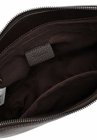 Interno di una borsa in pelle marrone scuro con una tasca con zip; foderatura in tessuto liscio, forma rettangolare e un'etichetta in pelle testurizzata.