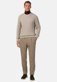 Pull gris clair à côtes avec un col rond, associé à un pantalon plissé beige. Le modèle porte des chaussures foncées. Design simple et ajusté.