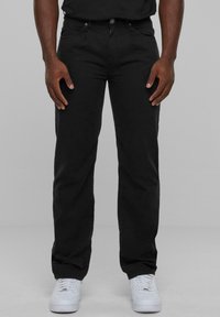 Pantalon noir en mélange de coton, coupe droite, avec poches avant et fermeture à bouton. Associé à des baskets blanches.