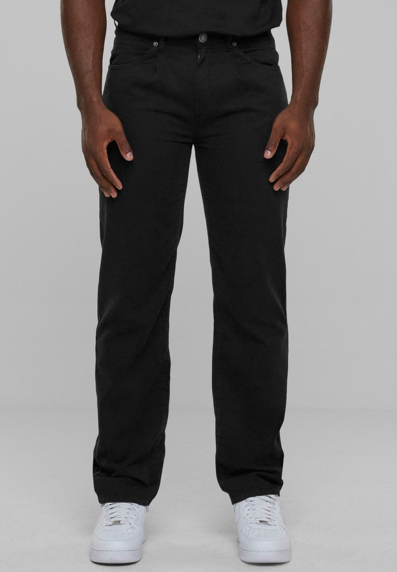 Pantalon noir en mélange de coton, coupe droite, avec poches avant et fermeture à bouton. Associé à des baskets blanches.