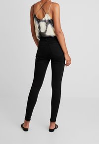 Jeans slim negros de cintura alta, combinados con una camiseta sin mangas de estampado tie-dye de color claro, con tirantes finos y diseño de espalda descubierta.