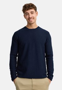 Maglietta a maniche lunghe di colore blu navy in un morbido tessuto a maglia, con scollo rotondo e polsini a coste. Il design presenta un orlo dritto e un sottile dettaglio con logo.