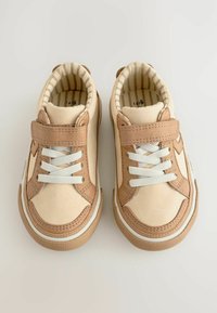 Baskets beiges et brunes avec des lacets blancs et une sangle Velcro. Dessus en simili cuir lisse, semelle texturée et doublure intérieure rayée.