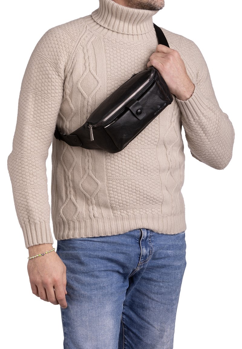 Marsupio in pelle nera con chiusura zip, dettaglio con bottone frontale e cintura regolabile, indossato sopra un pull beige chiaro.