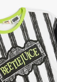 Vit t-shirt med svarta ränder och gröna detaljer. Har en framträdande svart och grön "BEETLEJUICE" grafik. Materialet är bomull.