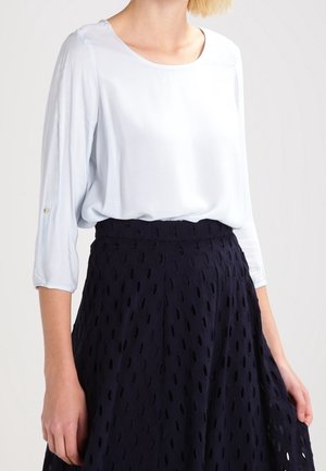 Blusa azzurro chiaro con maniche tre quarti, scollatura rotonda, tessuto morbido. Abbinata a una gonna blu navy con un motivo a intagli e design svasato.