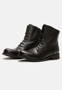 Botines de piel negra con un acabado suave, que cuentan con una puntera redondeada, parte delantera con cordones y un pequeño tacón apilado.
