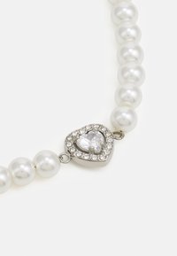 Collar de perlas que presenta perlas redondas y brillantes, con un cierre en forma de corazón de plata adornado con una gema transparente rodeada de pequeñas stras.