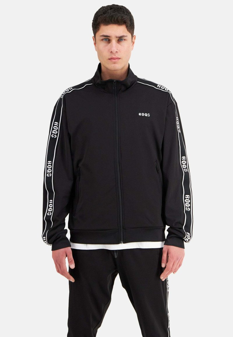 Schwarze Sport-Zipjacke mit weißem Logo und seitlichen Streifen. Sie verfügt über lange Ärmel, einen hohen Kragen und eine glatte Textur.