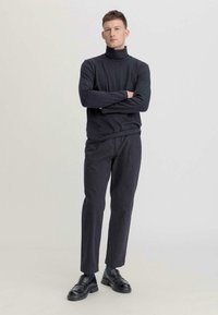 Schwarzer Rollkragenpullover aus weichem Material, kombiniert mit dunklen Hosen und schwarzen Slippern. Einfaches Design mit modernem Schnitt.