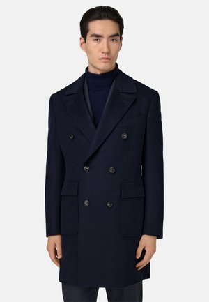 Marinblå ull dubbelknäppt kappa med slag, som har sex svarta knappar, två sidofickor och en slät yta.