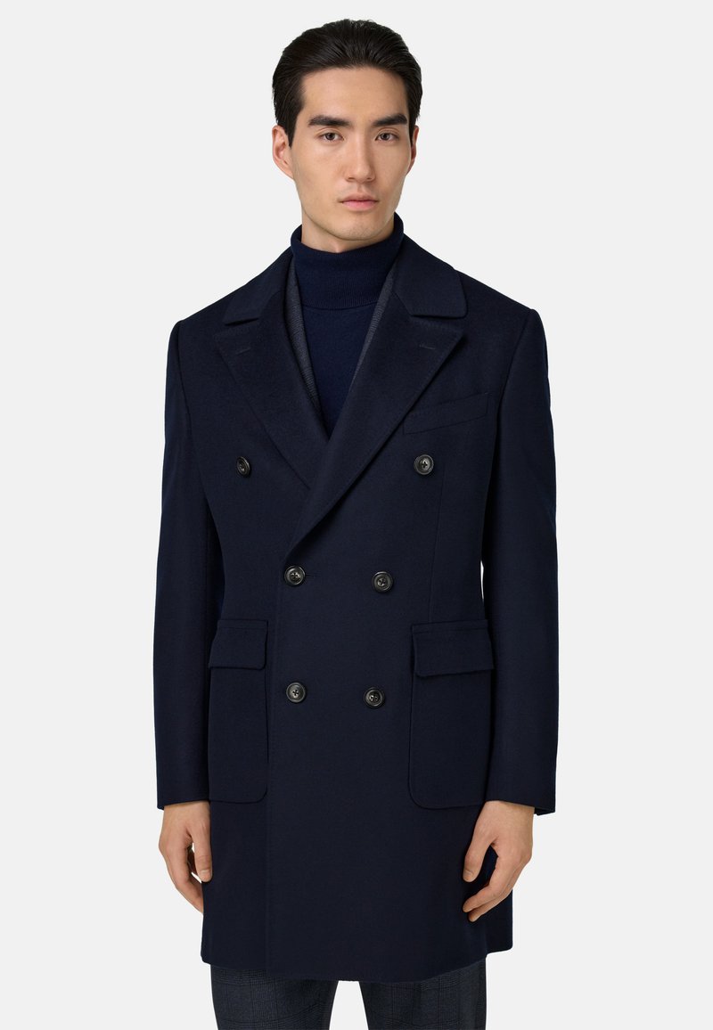 Abrigo de lana azul marino de doble botonadura con solapas muesca, que cuenta con seis botones negros, dos bolsillos laterales y una textura suave.