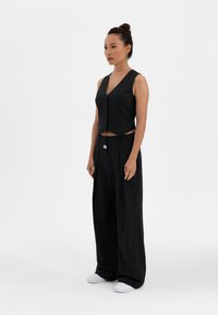 Black pinstriped cropped vest with buttons and high-waisted, wide-leg trousers. Soft texture, relaxed fit, paired with white sneakers.