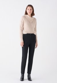 Suéter beige con un cuello ancho, combinado con pantalones negros de corte ajustado y botas de tobillo. Textura suave y diseño sencillo, adecuado para un estilo casual.