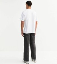 T-shirt bianca in cotone con scollo rotondo, abbinata a pantaloni larghi grigio scuro con tasche laterali e una finitura leggermente strutturata.