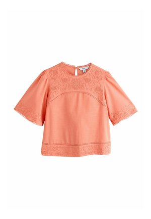 Korallinvärinen lyhythihainen pusero, jossa on kirjailtuja kukka- ja abstrakteja kuvioita rinnassa, hihoissa ja helmassa. Pyöreä pääntie ja taakse kiinnittyvä nepparikiinnitys.