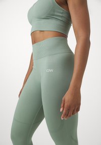 Ensemble de sport vert comprenant un soutien-gorge de sport ajusté et des leggings taille haute. Fabriqué en tissu extensible avec des accents côtelés et un détail de logo.