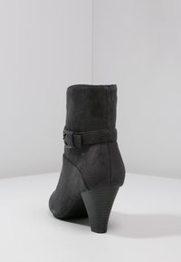 Bota de tobillo de ante gris con un diseño curvado, que presenta un detalle de hebilla y un tacón cónico. Textura suave con acentos de costura.