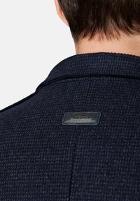 Granatowy płaszcz teksturowany z wyraźnym kołnierzem oraz czarną skórzaną metką z nazwą marki "LANCERTO" na plecach.