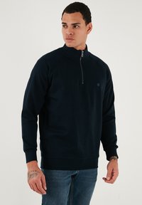 Sötétkék pulóver, magas gallérral és fél cipzárral. Puha anyagból készült, hosszú ujjú és laza fazonú.