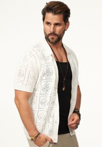 Weißes Kurzarm-Strickshirt mit strukturiertem Lochmuster. Kombiniert mit einem schwarzen Tanktop und gestapelten Halsketten.